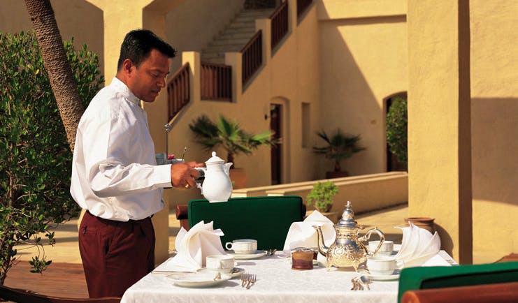 Al Maha Desert Resort and Spa Dubai outdoor dining waiter pouring tea at outdoor dining table