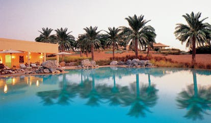 Al Maha Desert Resort and Spa Dubai pool with loungers umbrellas and palm trees