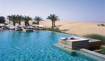 Bab Al Shams Desert Resort and Spa Dubai desert pool with umbrellas and palm trees