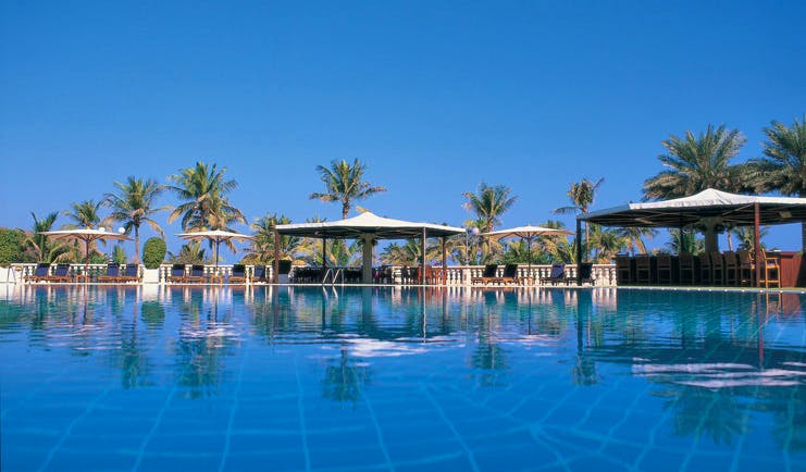 Al Bustan Palace Hotel Oman swimming pool with white umbrellas and loungers