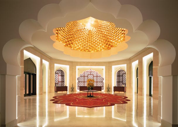 Hall area with white column pillars, a red rug and intricately detailed ceiling 