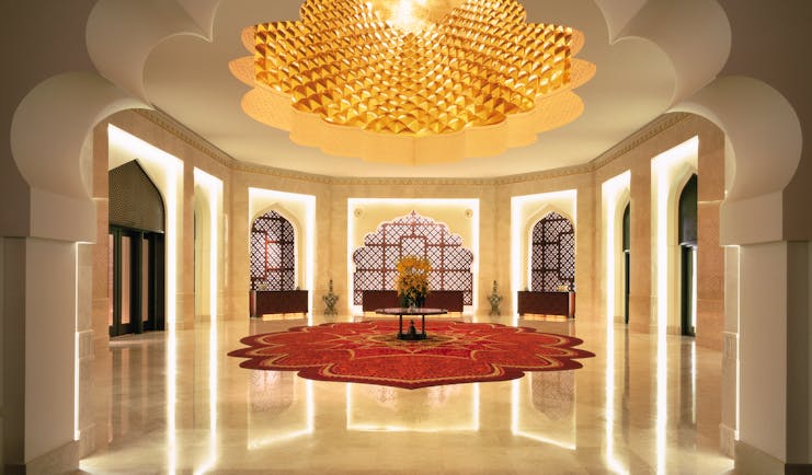 Hall area with white column pillars, a red rug and intricately detailed ceiling 