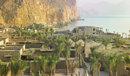 Six Senses Zighy Bay Oman aerial sea mountain view of complex of stone buildings palm trees mountain and sea