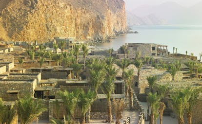 Six Senses Zighy Bay Oman aerial sea mountain view of complex of stone buildings palm trees mountain and sea