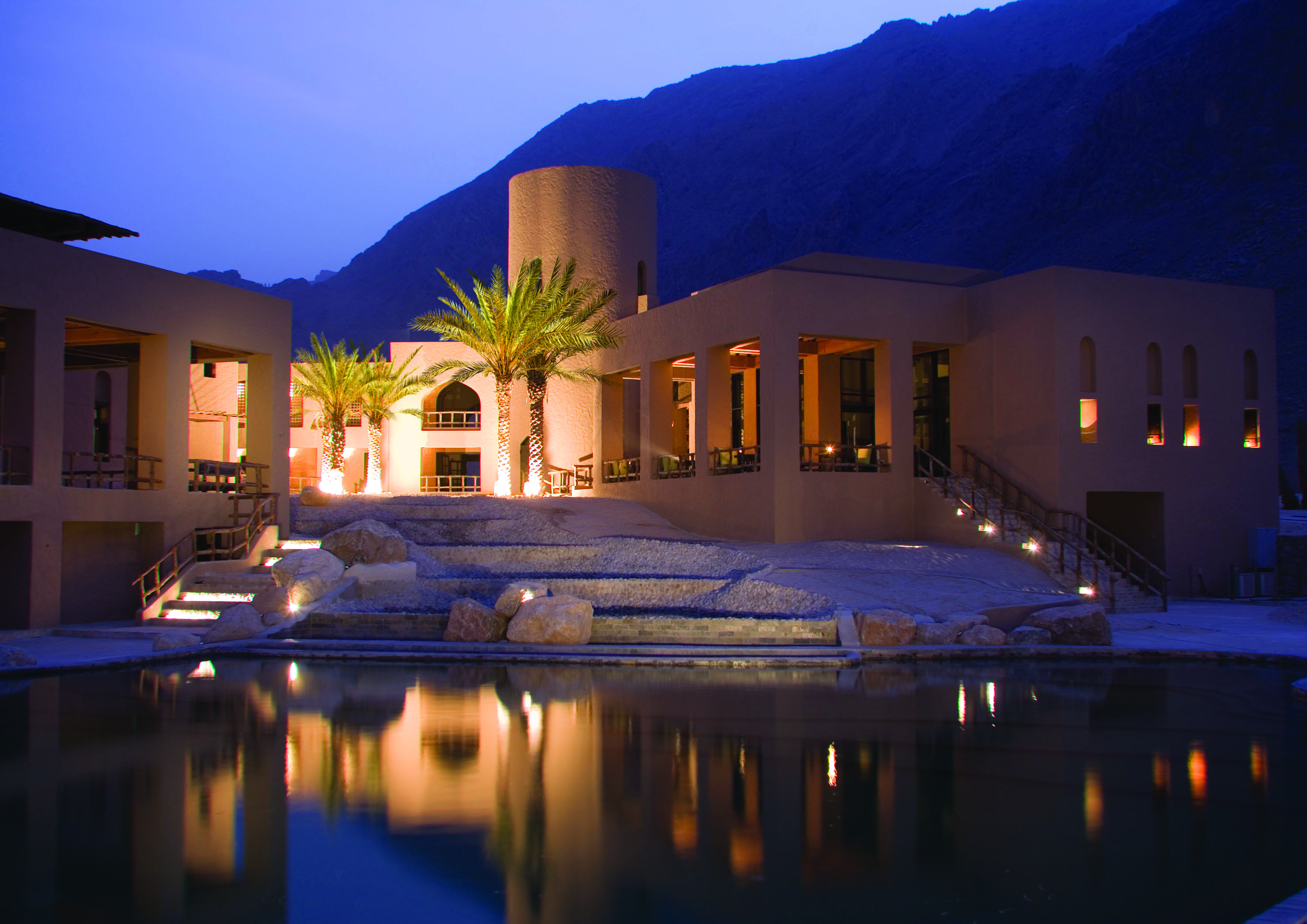 Six Senses Zighy Bay Oman exterior pool night  cream stone building with palms and pool