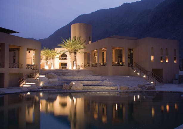 Six Senses Zighy Bay Oman exterior pool night  cream stone building with palms and pool