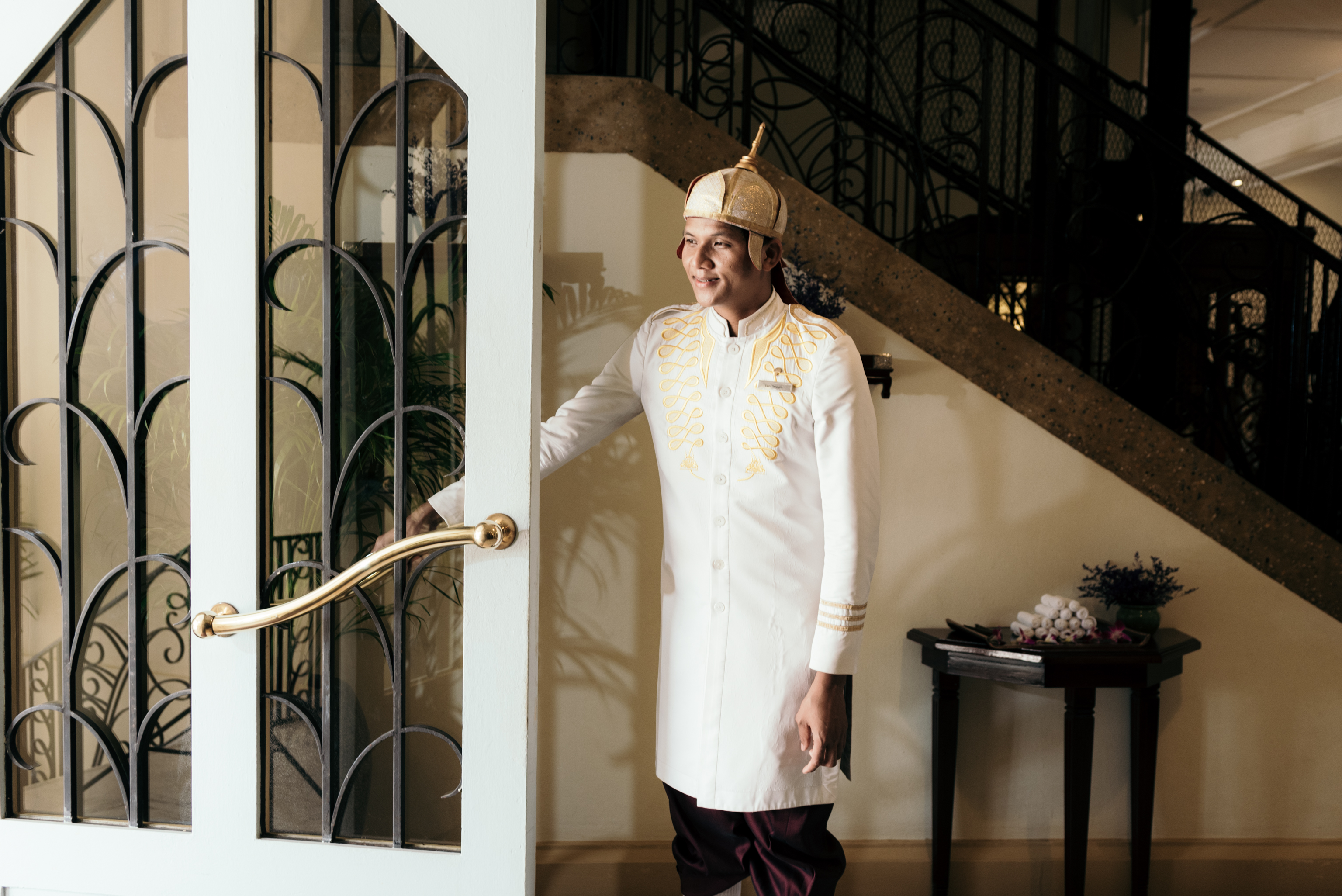 Man at door in white coat and hat holding open door