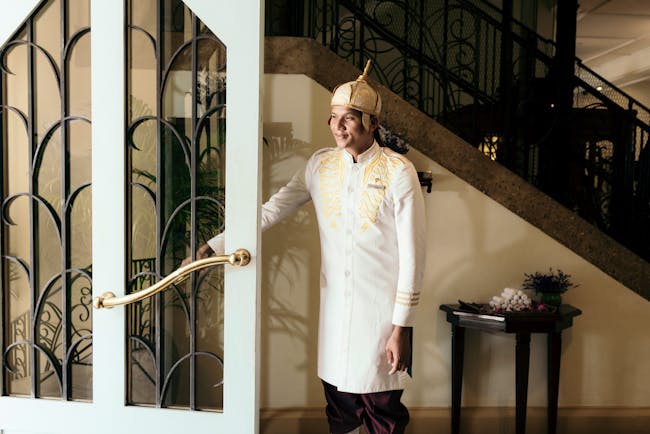 Man at door in white coat and hat holding open door