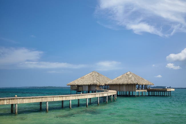 View of a restaurant at Songa Saa Private island with two beach huts on top of the sea with a bridge leading to them