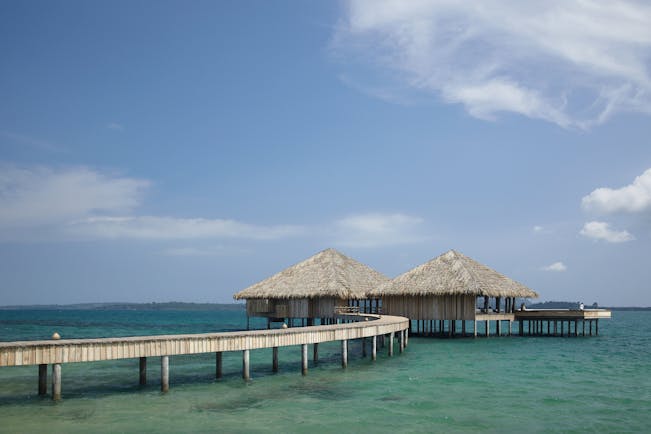 View of a restaurant at Songa Saa Private island with two beach huts on top of the sea with a bridge leading to them