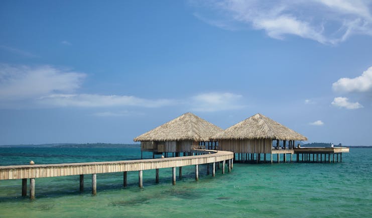 View of a restaurant at Songa Saa Private island with two beach huts on top of the sea with a bridge leading to them