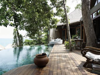 View of the exterior of a two bedroom villa at the Song Saa Private Island hotel with an infinity pool, wooden decking and sun loungers