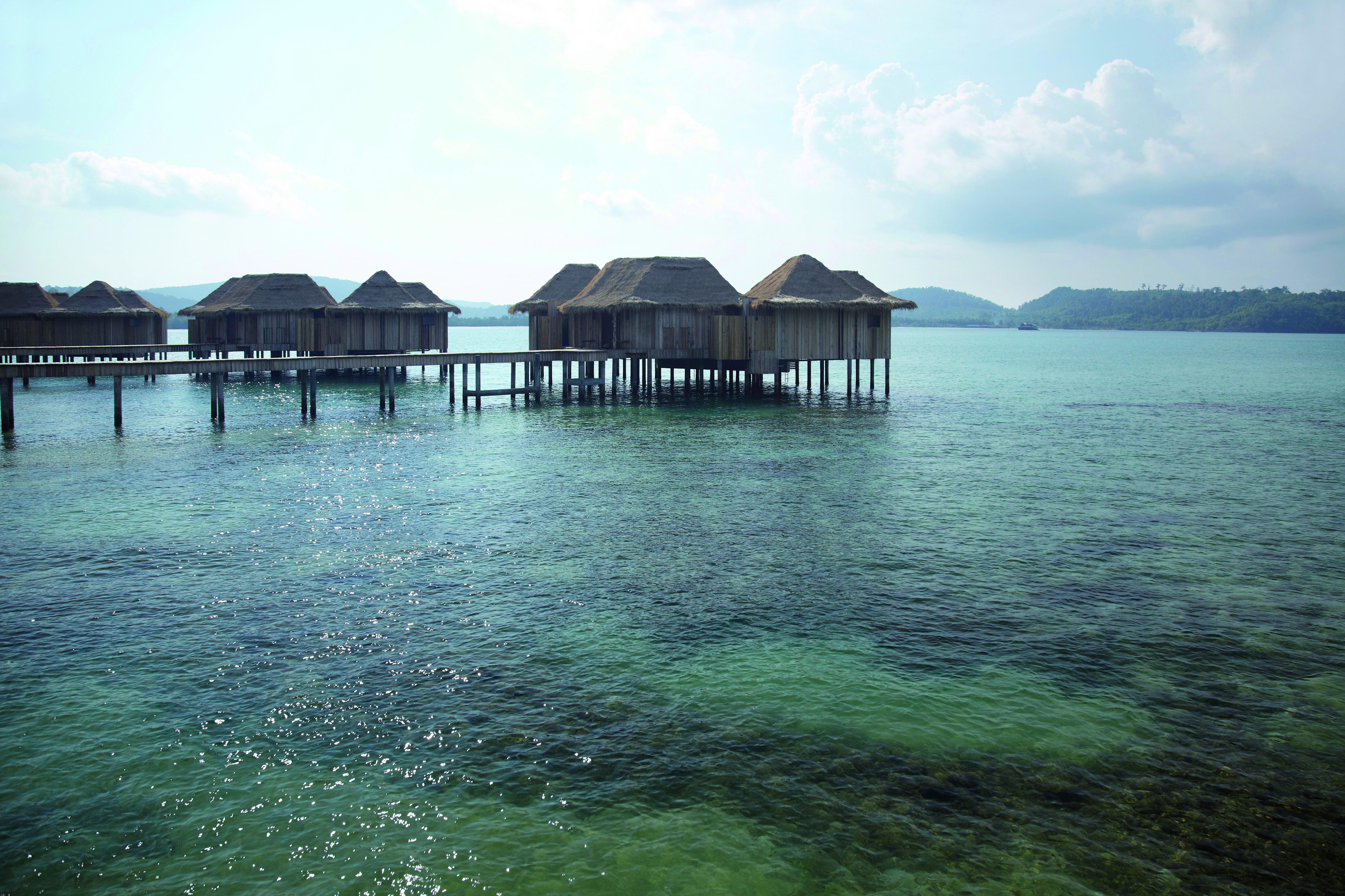 View of two bed overwater villas with the sea beneath them, bridges joining them up and the early morning sun in the sky