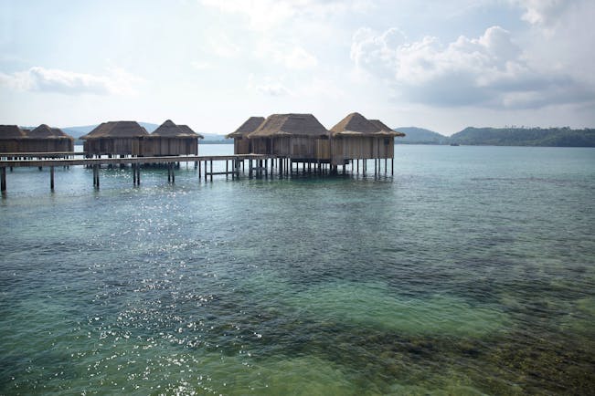 View of two bed overwater villas with the sea beneath them, bridges joining them up and the early morning sun in the sky