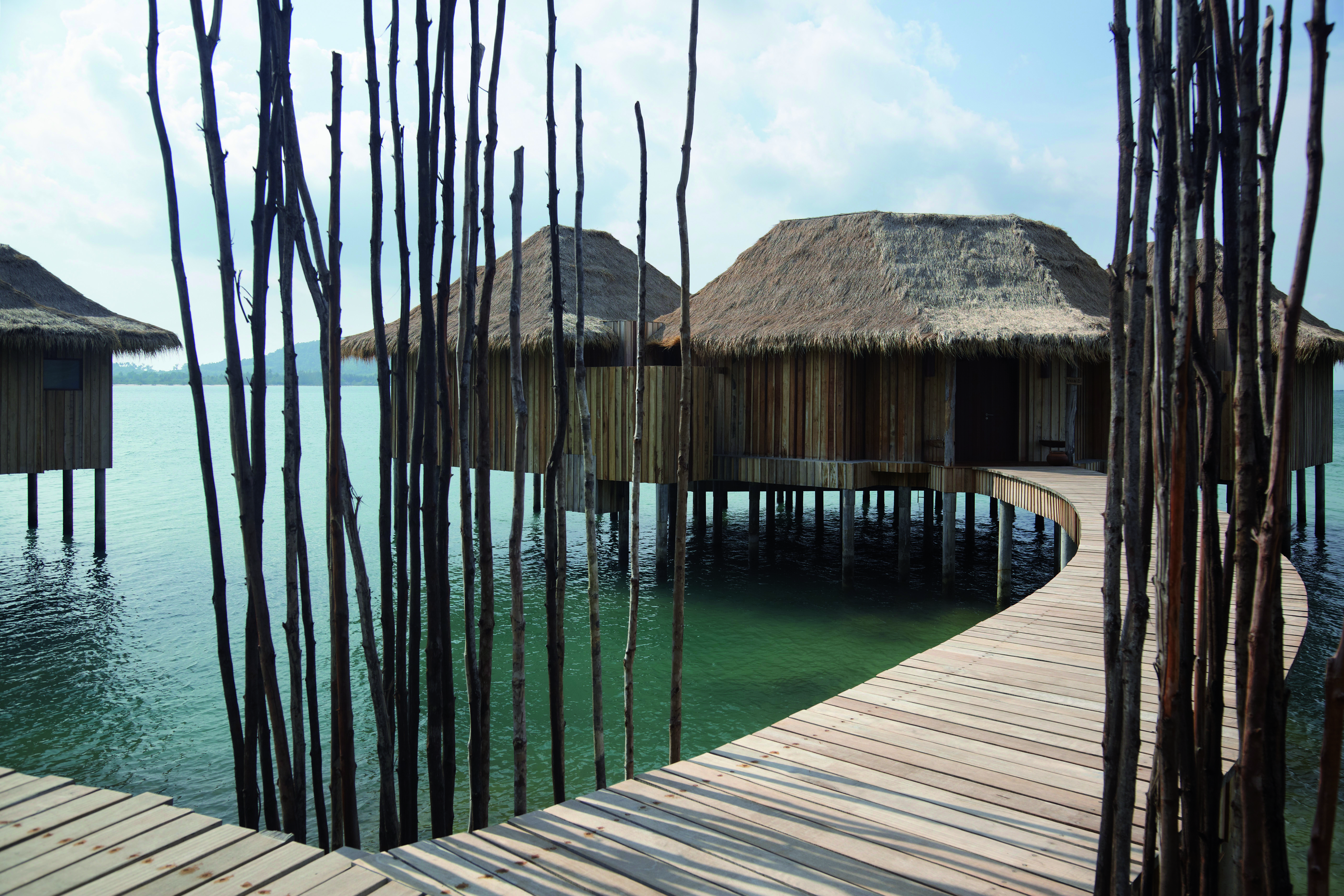 Exterior of the two bedroom overwater villas with beach hut style roof and wooden bridge over the sea to enter 