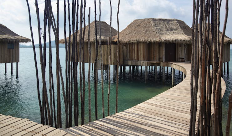 Exterior of the two bedroom overwater villas with beach hut style roof and wooden bridge over the sea to enter 
