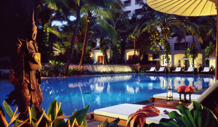 Anantara Siam Bangkok Thailand outdoor swimming pool loungers umbrellas garden pond night time 