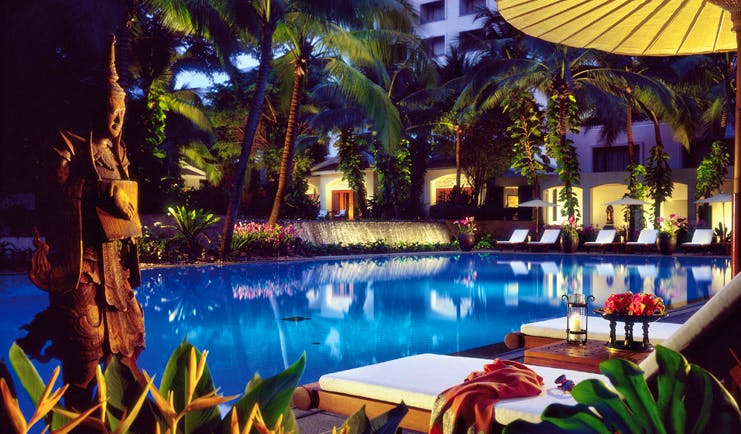 Anantara Siam Bangkok Thailand outdoor swimming pool loungers umbrellas garden pond night time 