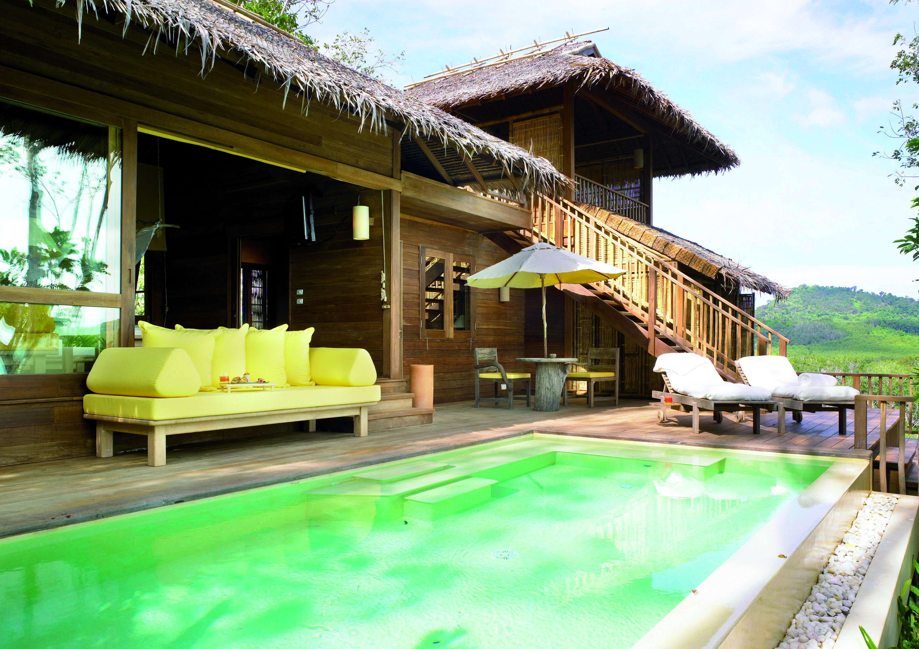 Exterior view of a deluxe villa at the Six Senses Yao Nai with a large rectangular pool with wooden decking area, seating areas with beach hut style buildings to the side