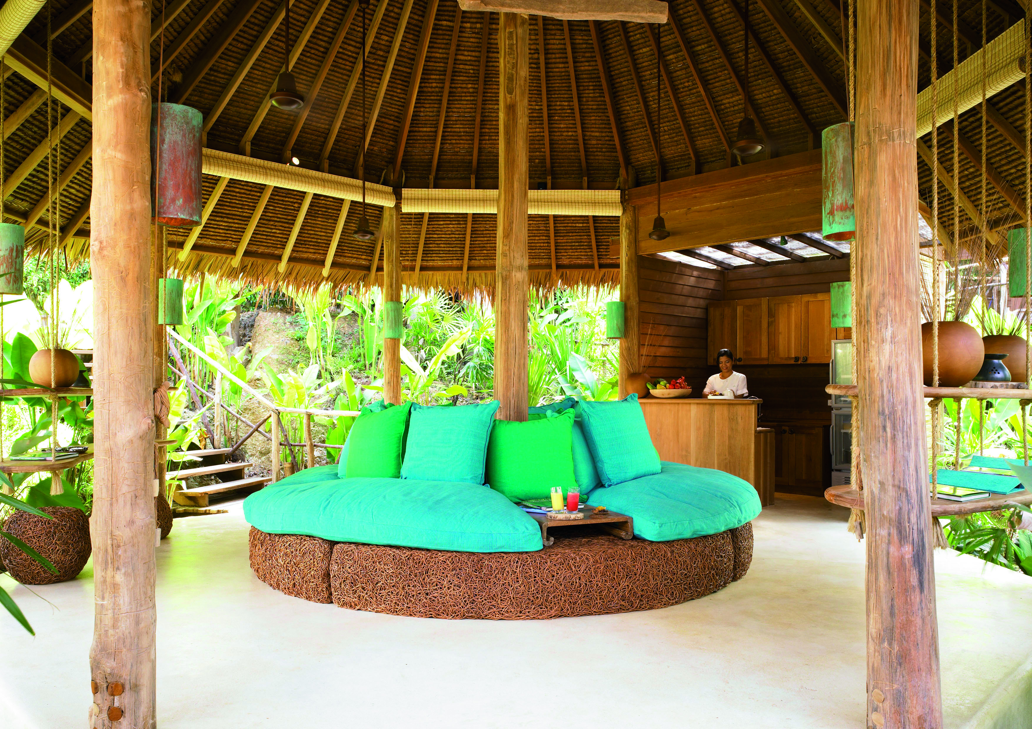 Six Senses Yao Nai spa juice bar in beach hut with blue and green sofa seating area, palm trees in the background and a wooden bar