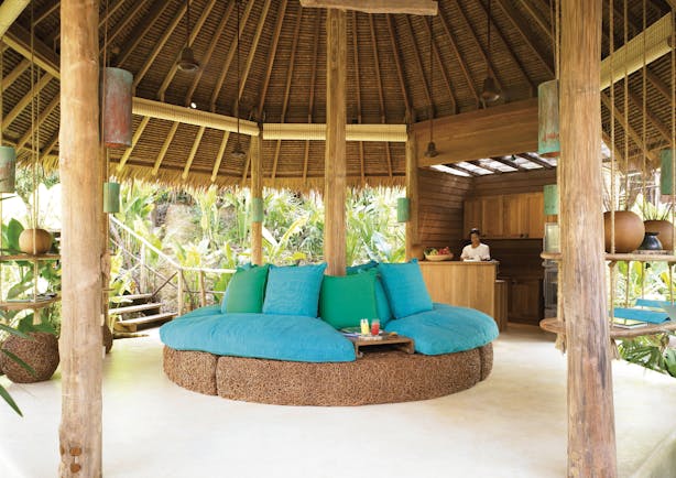 Six Senses Yao Nai spa juice bar in beach hut with blue and green sofa seating area, palm trees in the background and a wooden bar
