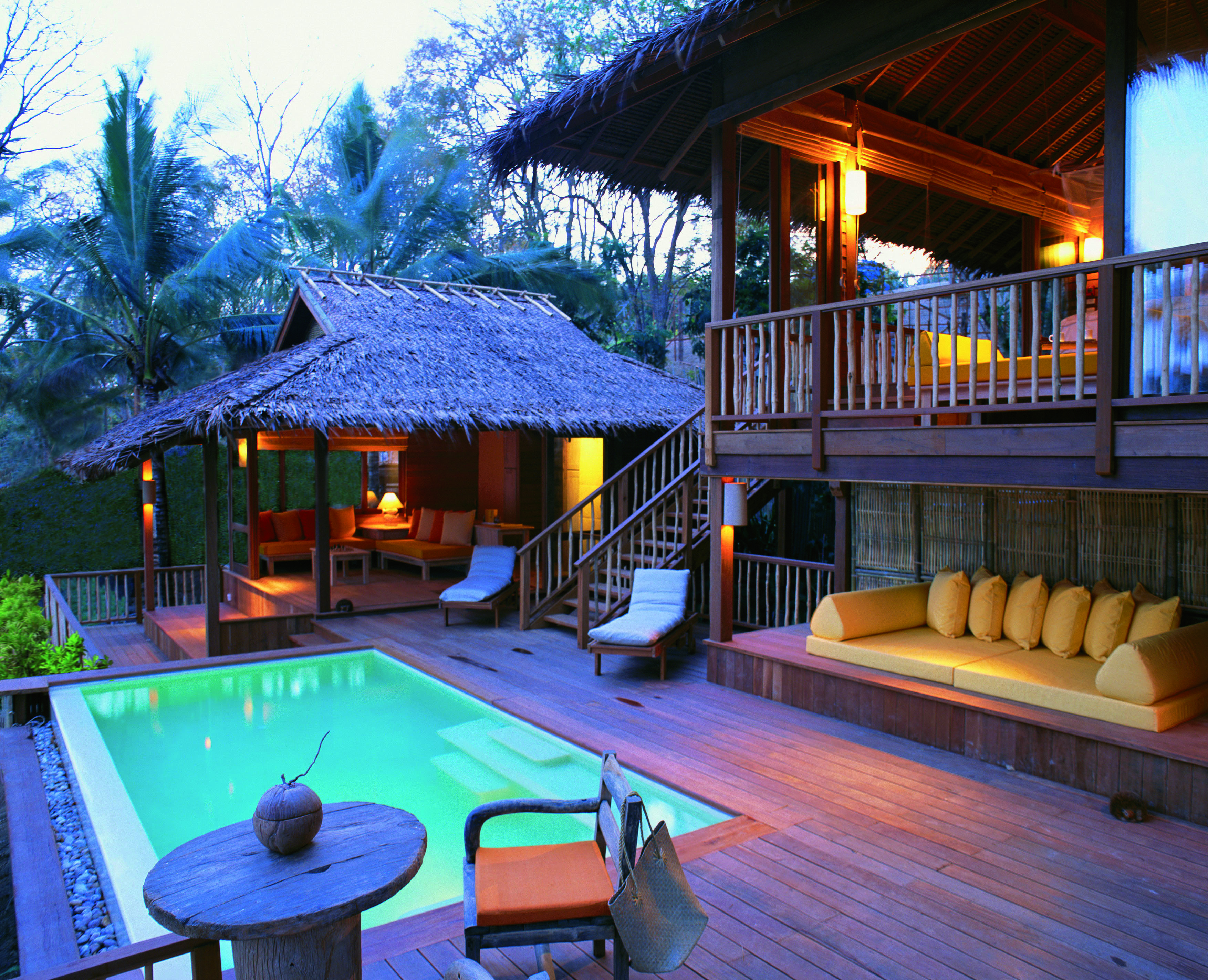 Exterior view of a villa at the Six Senses Yao Nai with a large rectangular pool, wooden decking, seating areas, a cream couch and wooden stairs leading up to the suite