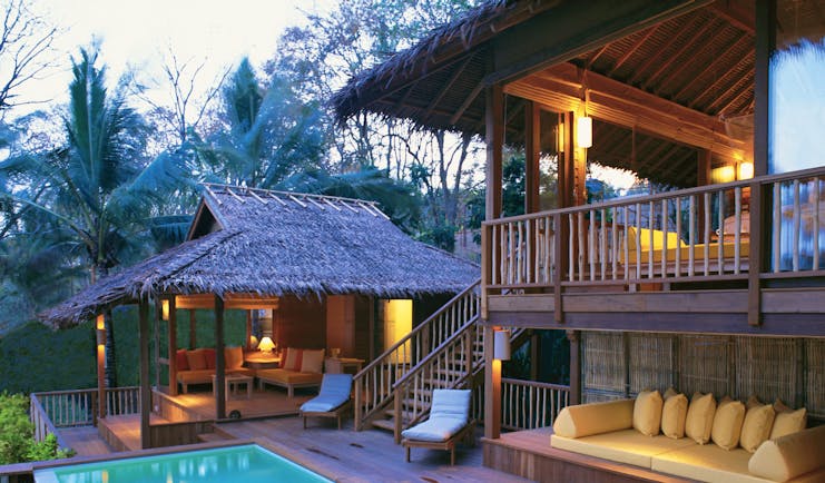 Exterior view of a villa at the Six Senses Yao Nai with a large rectangular pool, wooden decking, seating areas, a cream couch and wooden stairs leading up to the suite
