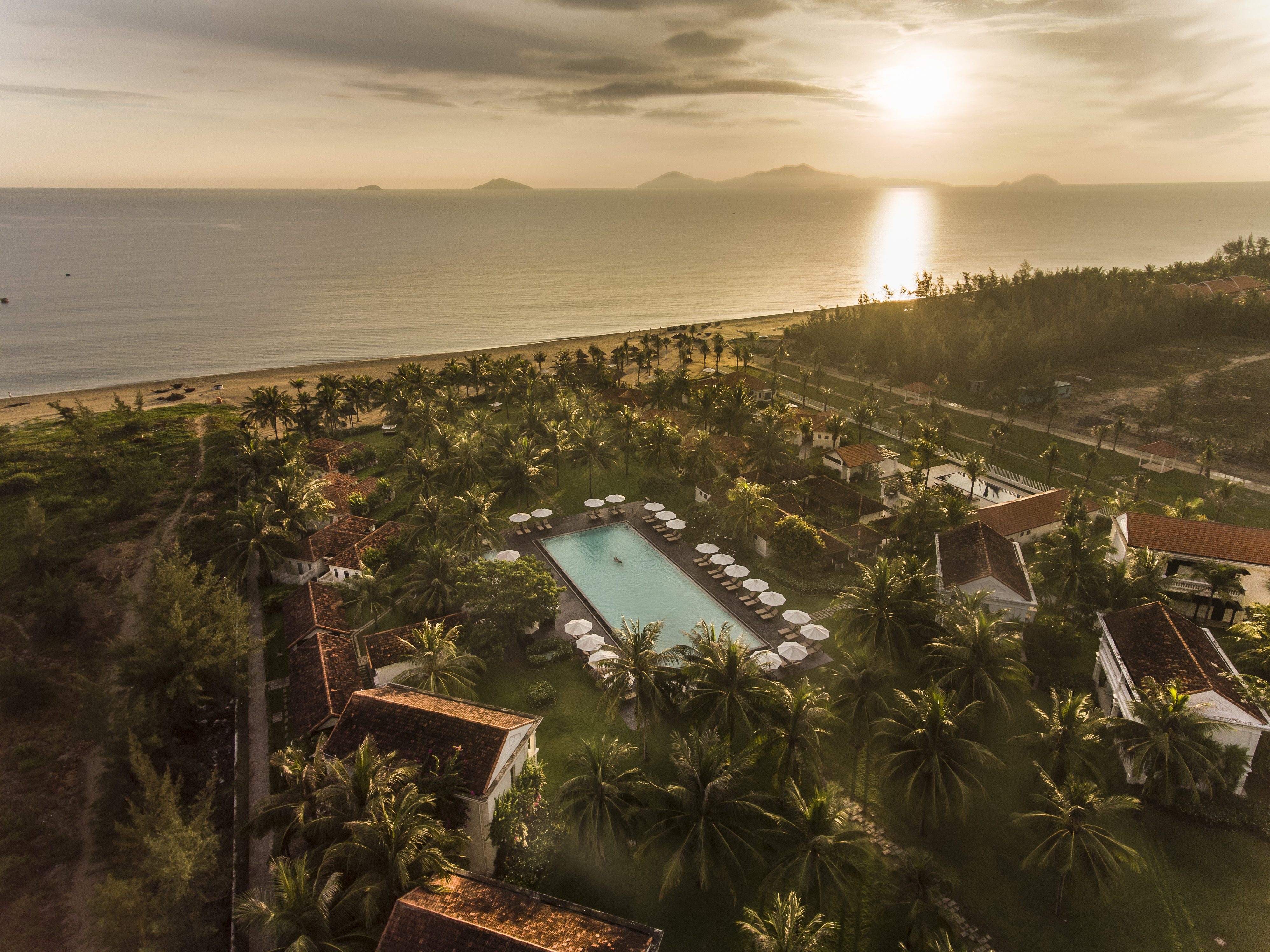 Boutique Hoi An resort aerial shot, villas, pool, beach in background, palm trees and greenery
