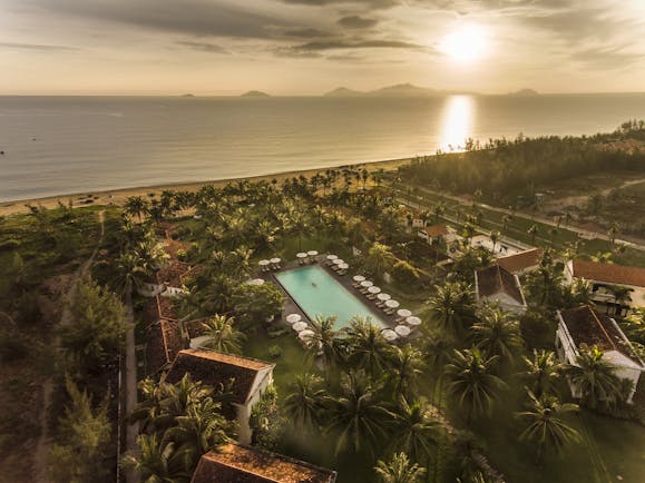 Boutique Hoi An resort aerial shot, villas, pool, beach in background, palm trees and greenery