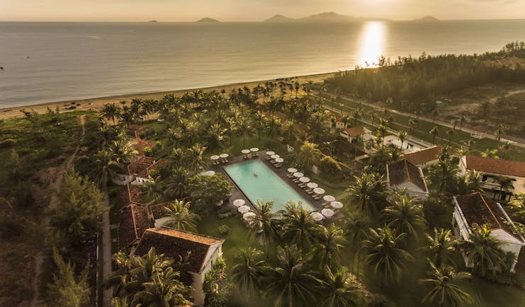 Boutique Hoi An resort aerial shot, villas, pool, beach in background, palm trees and greenery
