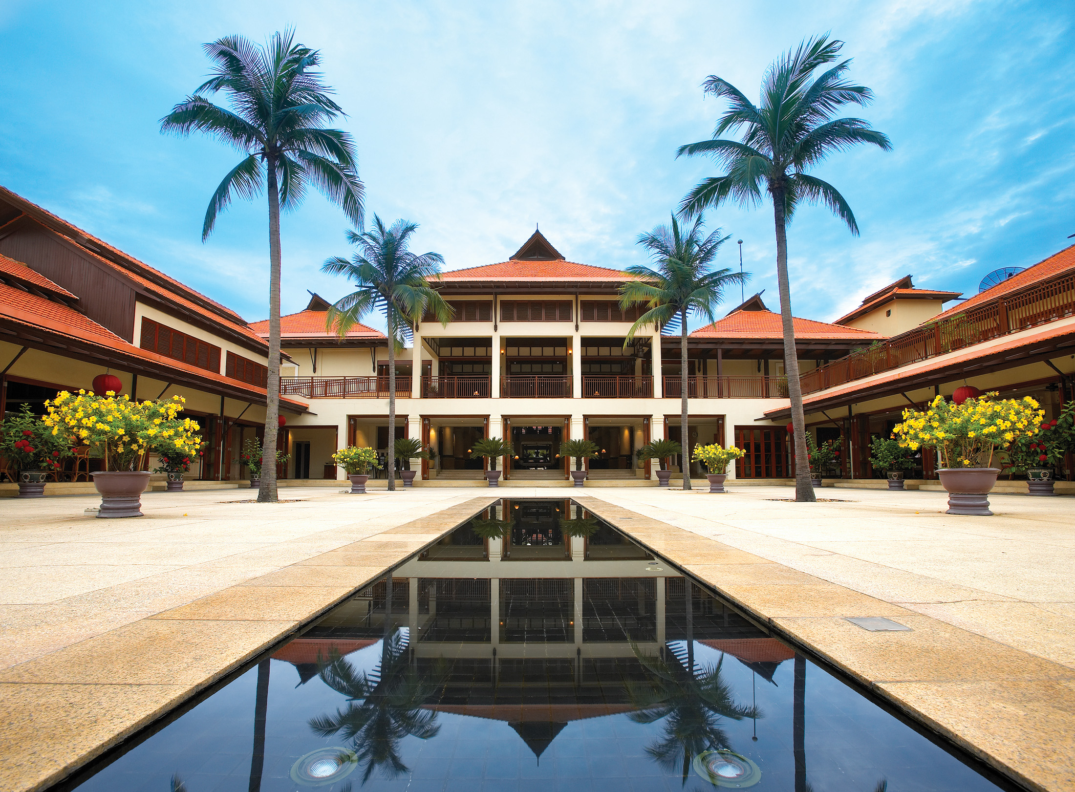 Furama Resort Vietnam building with white portico and two palms behind narrow pool