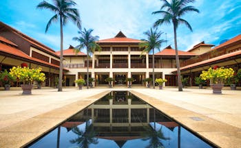 Furama Resort Vietnam building with white portico and two palms behind narrow pool