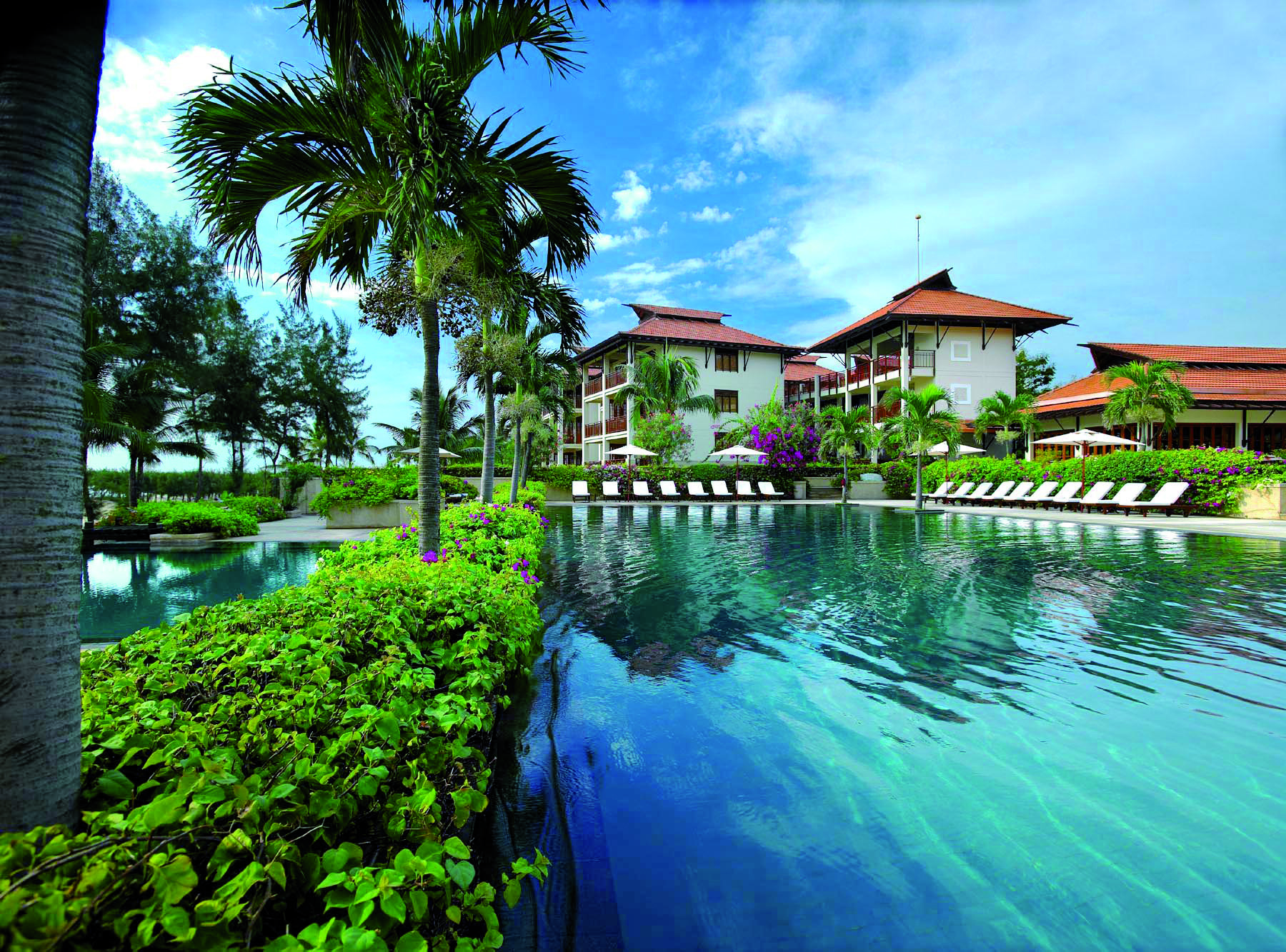 Furama Resort Vietnam large blue swimming pool with palm trees and white and red roofed building of 3 floors