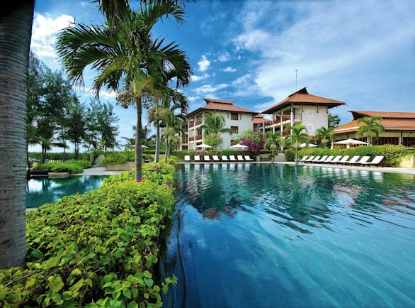 Furama Resort Vietnam large blue swimming pool with palm trees and white and red roofed building of 3 floors