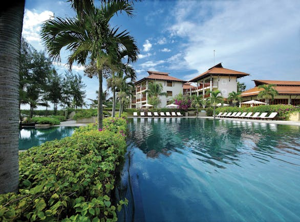 Furama Resort Vietnam large blue swimming pool with palm trees and white and red roofed building of 3 floors