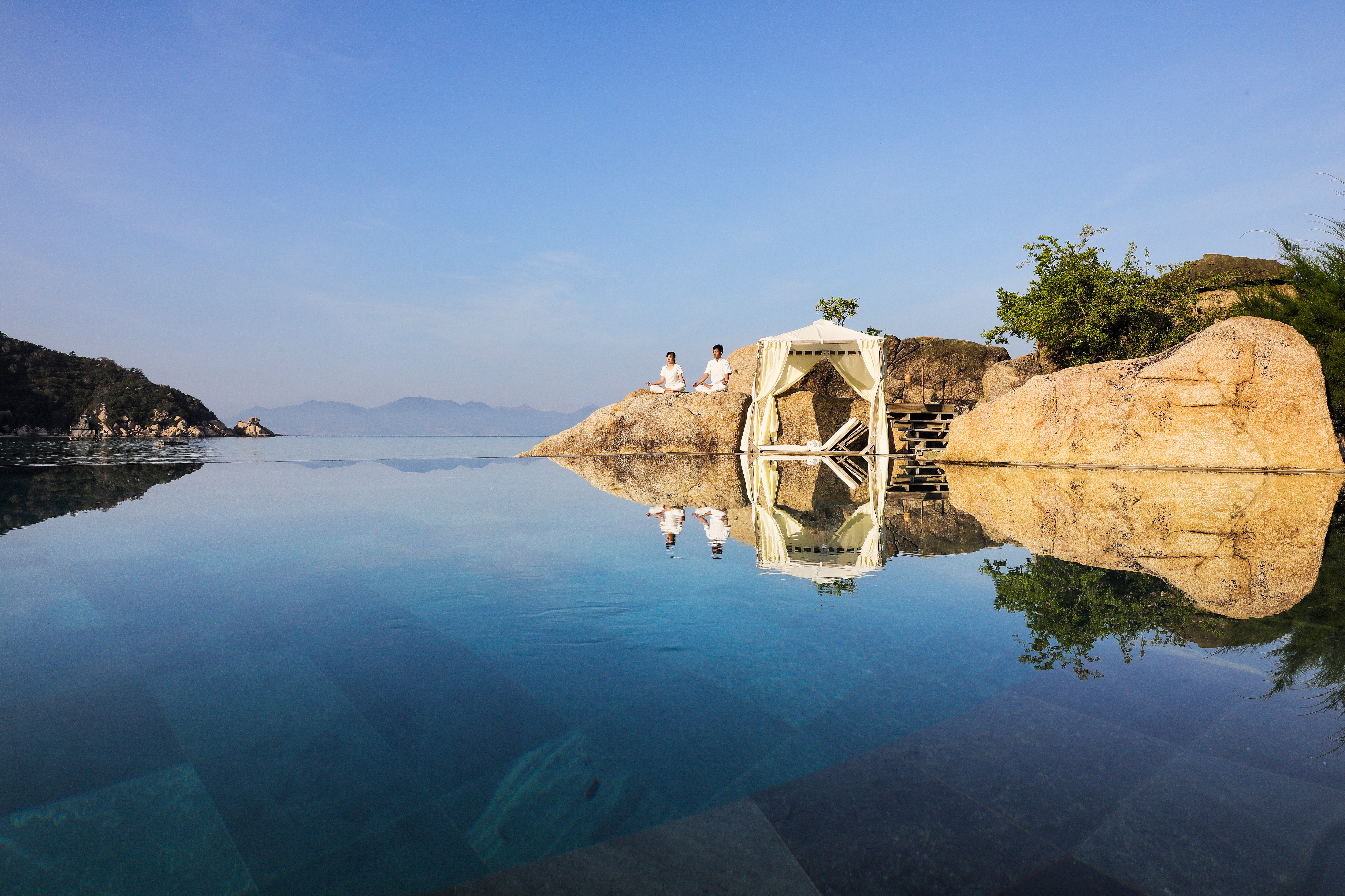 L'Ayla Ninh Van Bay infinity pool with mountains in background, couple meditating on rock