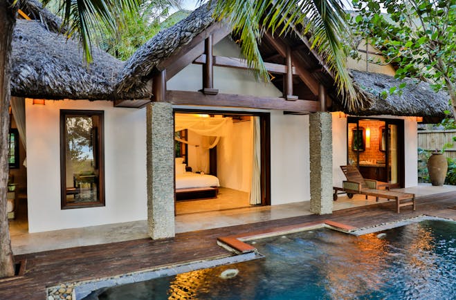 L'Ayla Ninh Van Bay villa exterior, pool, thatchted roof, palm trees, lit up bedroom