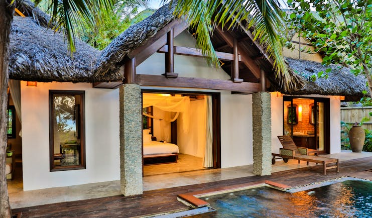 L'Ayla Ninh Van Bay villa exterior, pool, thatchted roof, palm trees, lit up bedroom