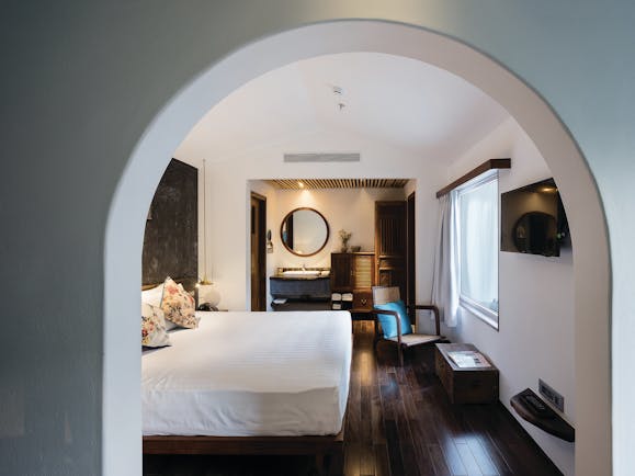 City room at the Myst Dong Khoi in Vietnam with a large archway entrance, big double bed, television, wooden floors and double doors leading into a bathroom 