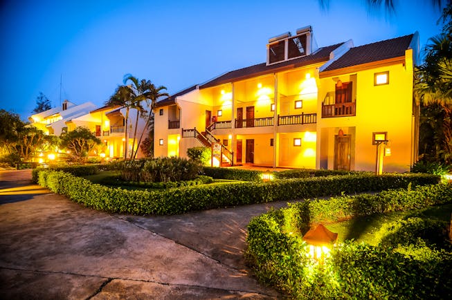 Palm Garden Resort exterior, hotel buildings lit up at night, pathways through neat gardens