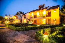 Palm Garden Resort exterior, hotel buildings lit up at night, pathways through neat gardens