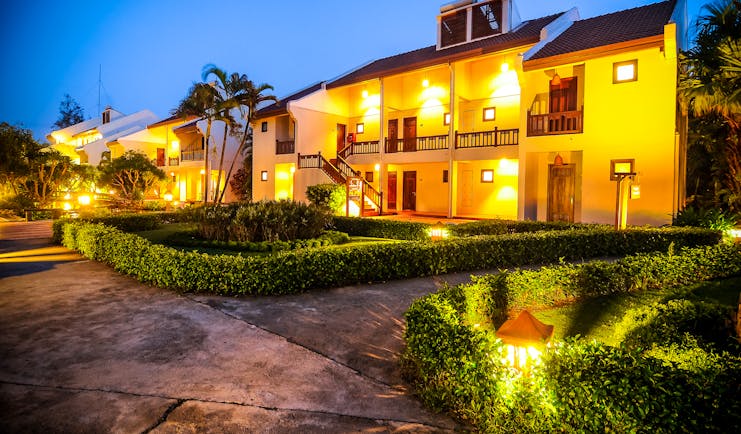 Palm Garden Resort exterior, hotel buildings lit up at night, pathways through neat gardens