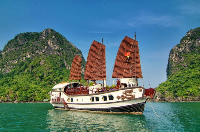 Red Dragon Junk boat on water, white boat with red sails, dragon on boat, rock formation in background