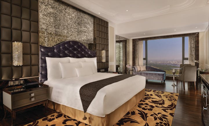 View of a deluxe room at the Reverie Saigon with a large bed, leopard print rug, television and big windows with a view over vietnam 