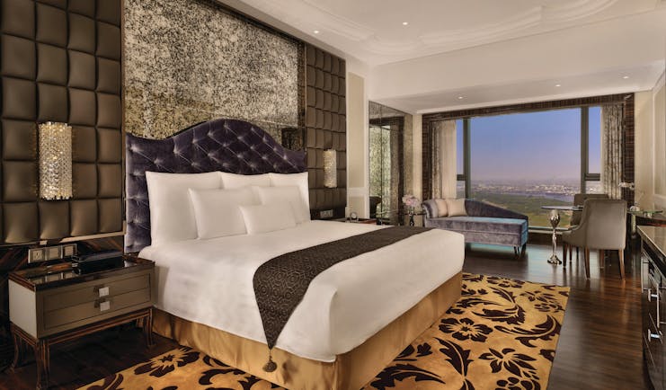 View of a deluxe room at the Reverie Saigon with a large bed, leopard print rug, television and big windows with a view over vietnam 