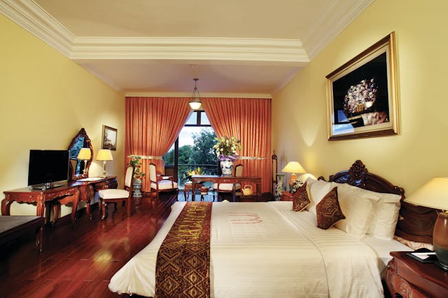 Colonial suite at the Saigon Morin Hotel with large bed, a television, paintings with gold frames and a yellow and red colour scheme