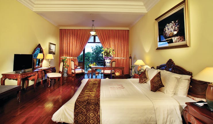 Colonial suite at the Saigon Morin Hotel with large bed, a television, paintings with gold frames and a yellow and red colour scheme