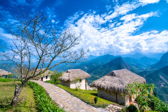 Topas Ecolodge bungalow exteriors, thatched buildings, mountain peaks in background, blue sky, green lawns