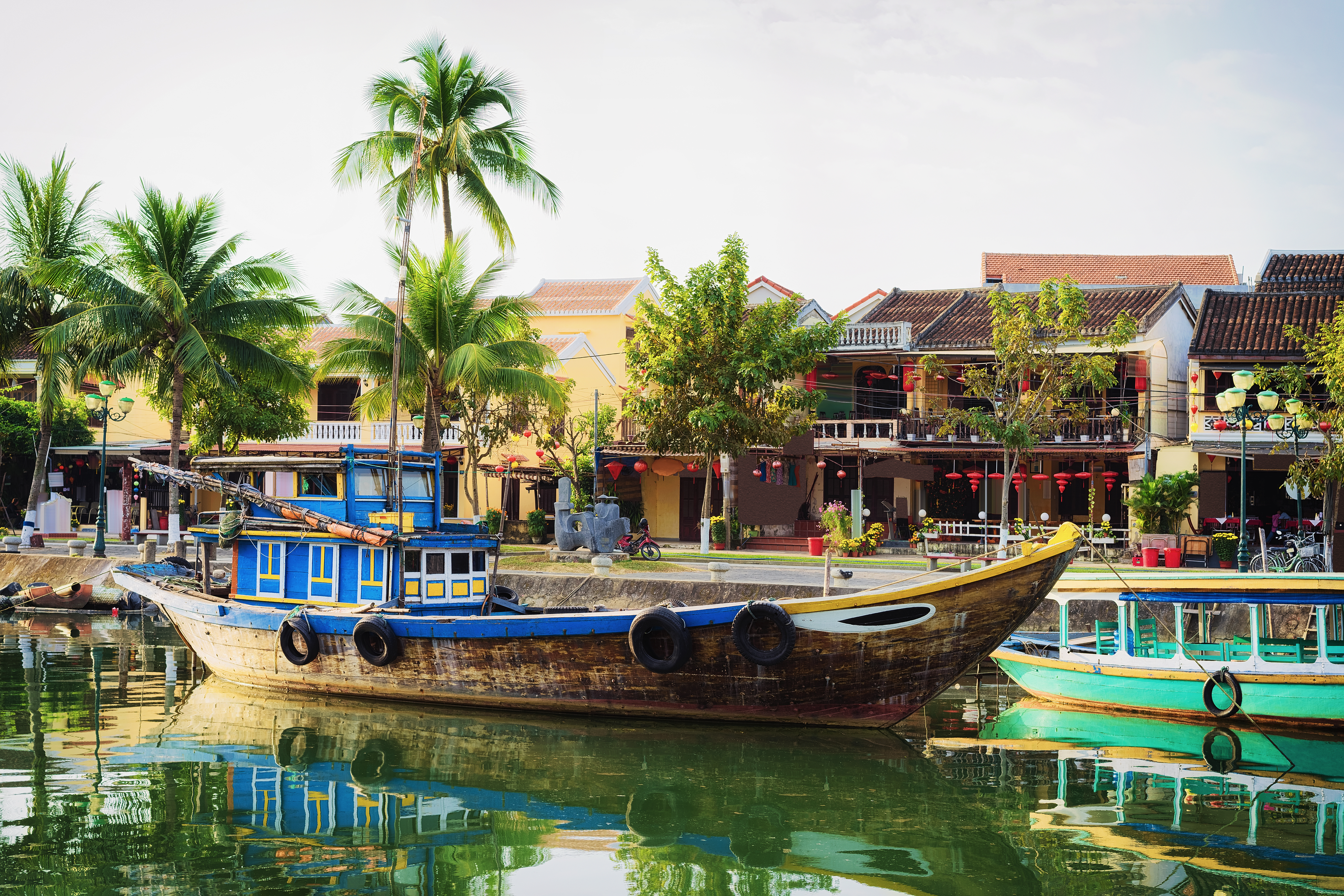 Wooden boat moored up Thu Bon River in Hoi An, riverside houses, palm trees