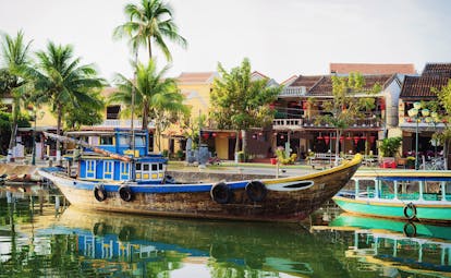 Wooden boat moored up Thu Bon River in Hoi An, riverside houses, palm trees